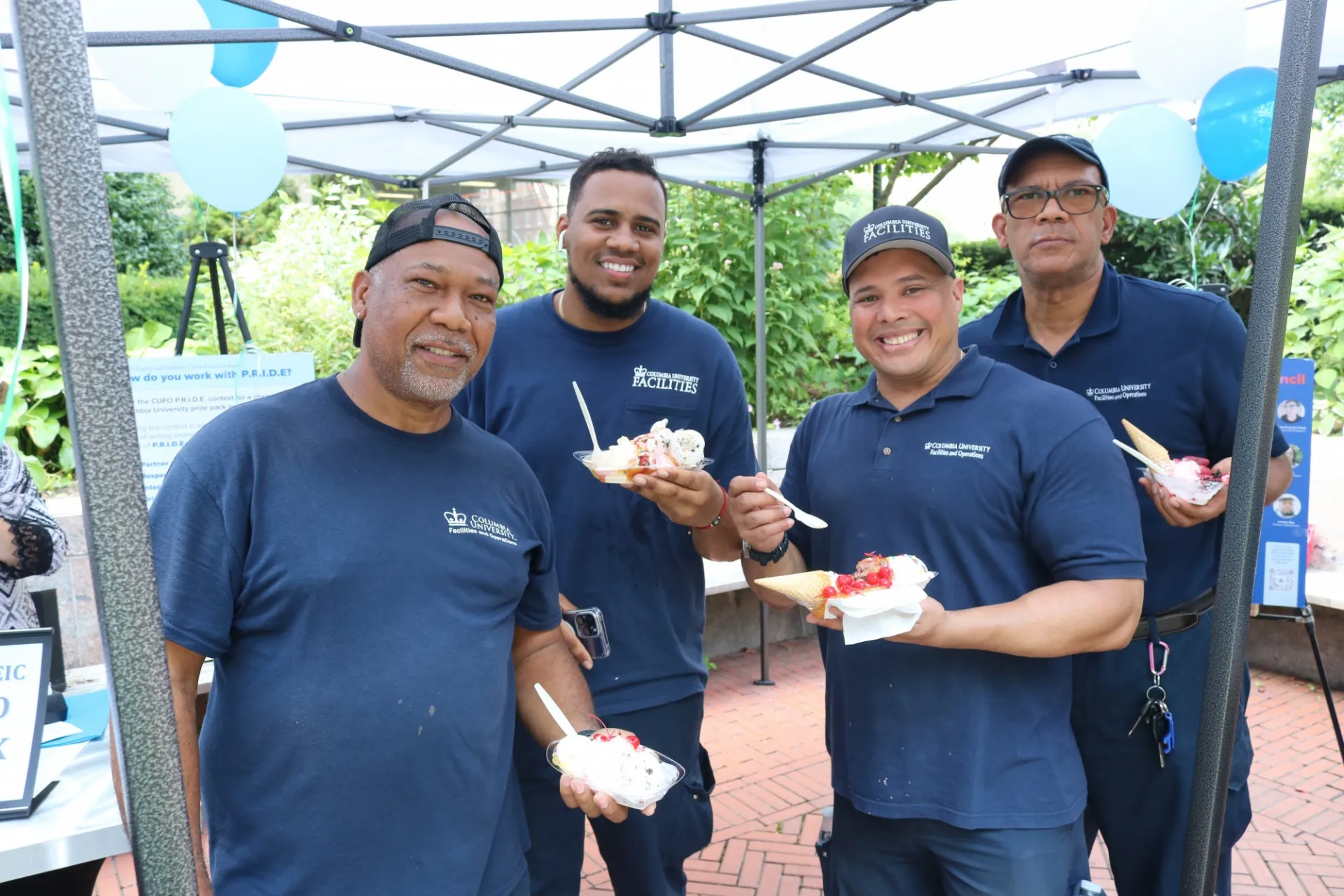 Employees with ice cream sundaes stand together underneath a tent.