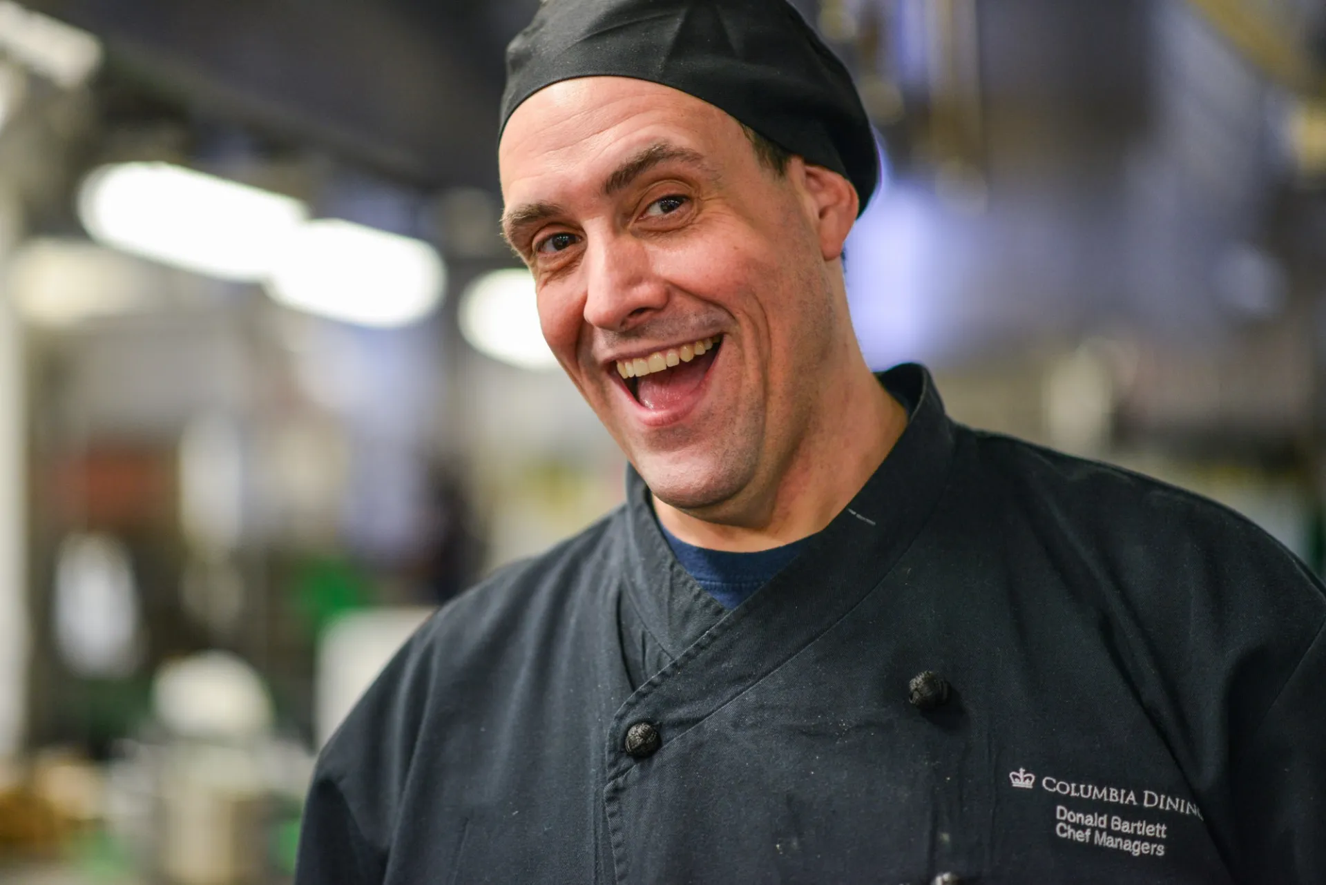 Chef Don smiles and poses for the camera, wearing a black chef's outfit. 