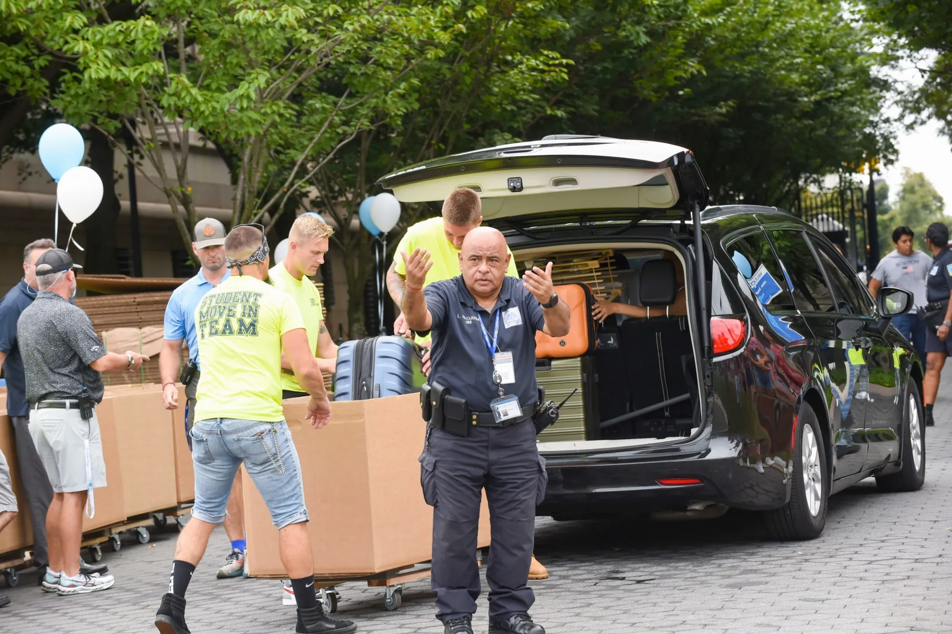 A team of movers get luggage out of someone's SUV while a Public Safety officer directs traffic on College Walk.